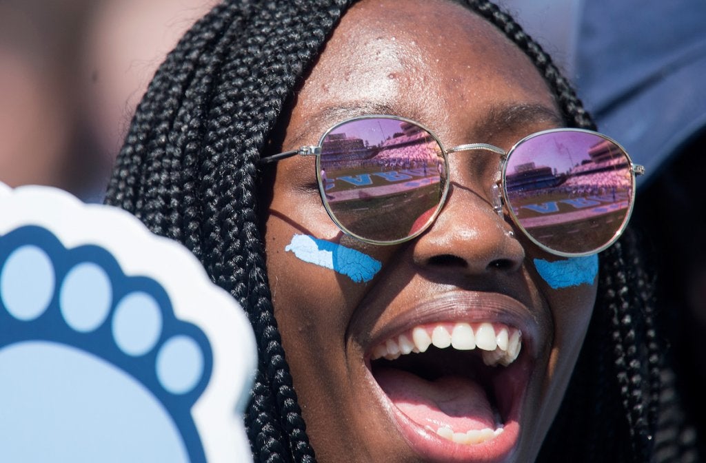 A black female student holding a Tar Heel-shaped foam finger cheers on the U.N.C. football team.