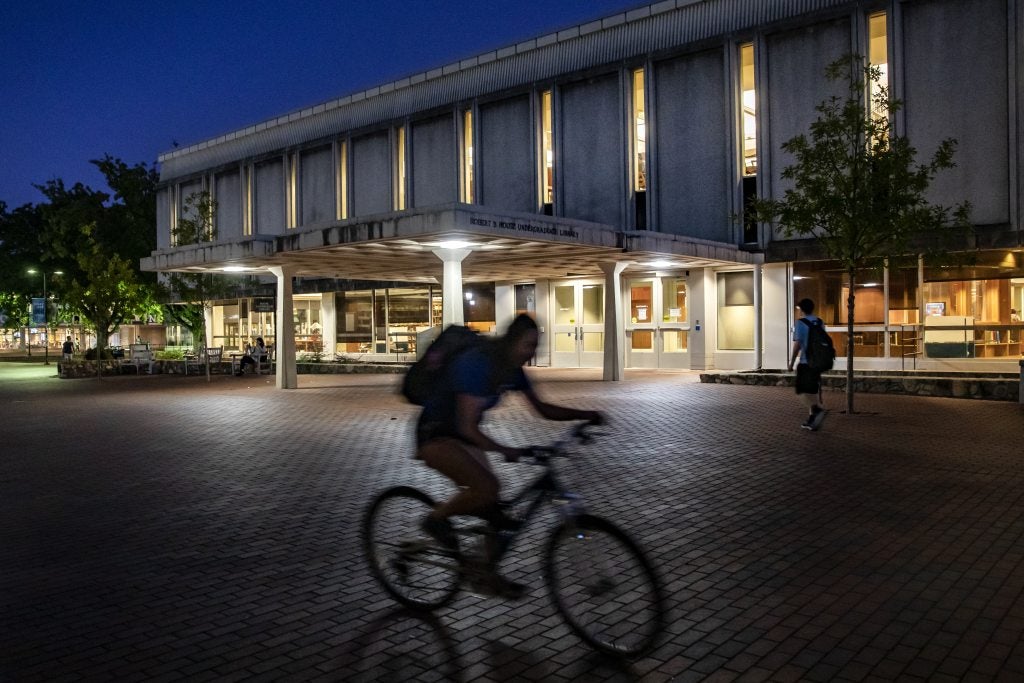 Nighttime photo of a biker riding by the Robert B. House Undergraduate Library on the campus of UNC-Chapel Hill.