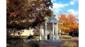 The Old Well on the campus of UNC-Chapel Hill on a sunny fall day. In the background are trees with varying shades of leaves.