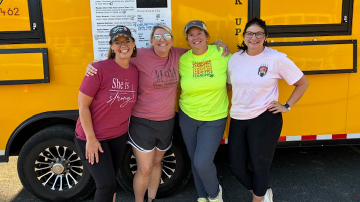 Four individuals standing next to yellow school bus.