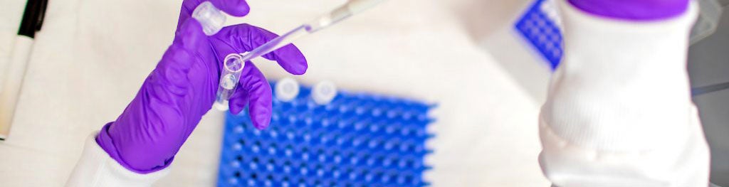 Gloved hands putting liquid into vial.