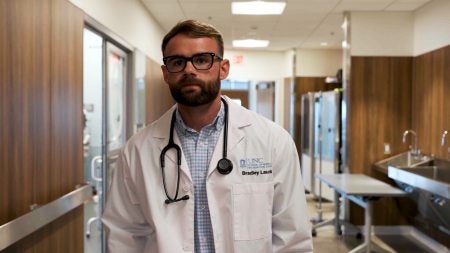 Bradey Lauck walking down hallway of a medical simulation lab in white coat.