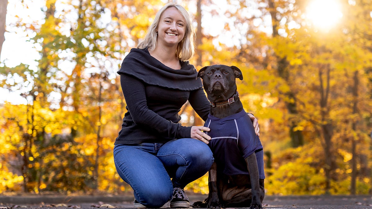 Caitlin Russell poses with her dog in front of fall leaves