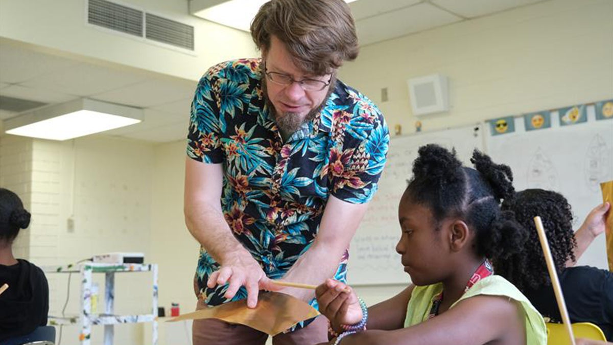 A Carolina Community Academy teacher helps a student work on the leaves for a class project building a mural.