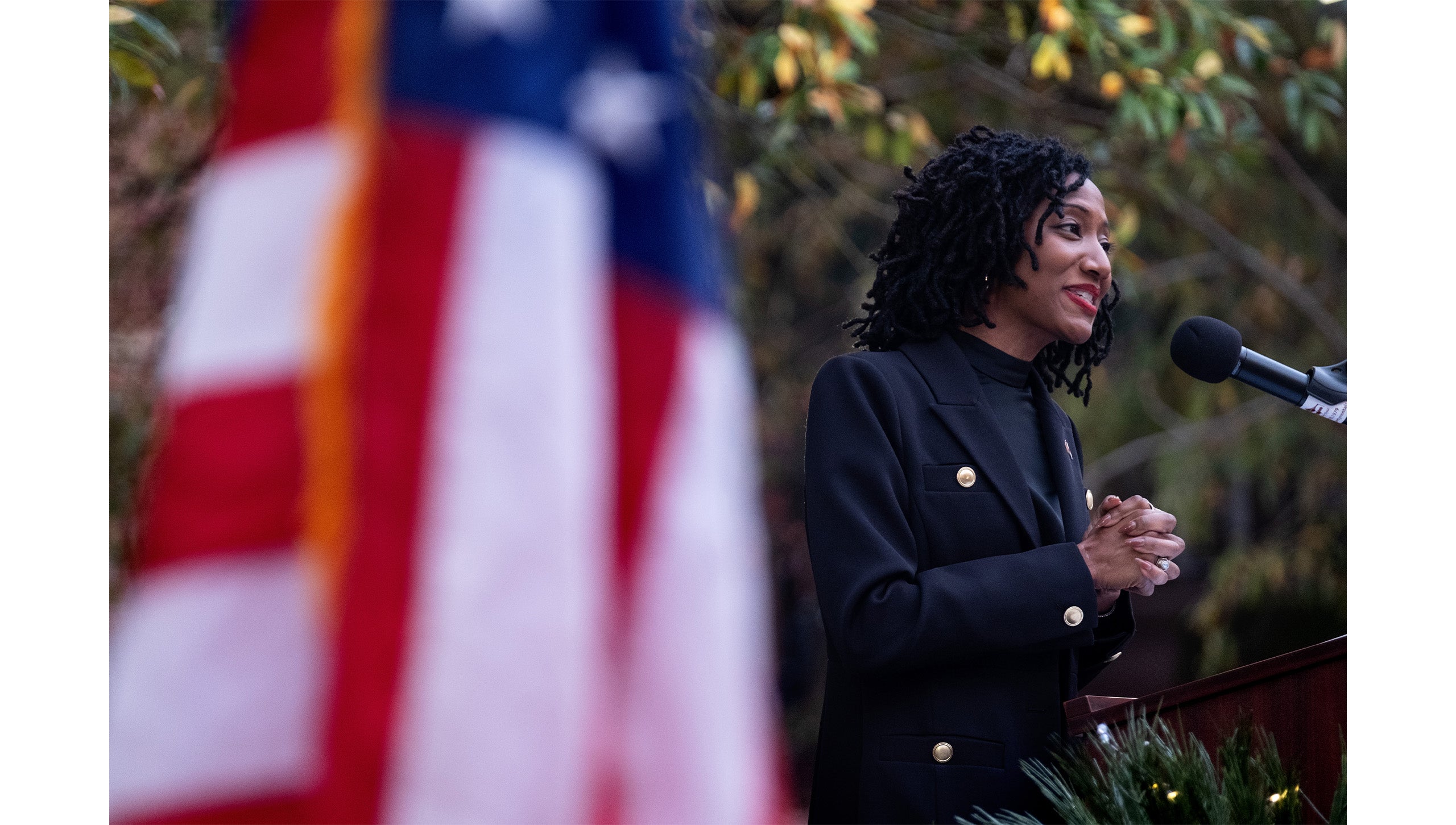 Jocelyn Mitnaul Mallette speaking into a microphone at a podium during the grand opening of the UNC-Chapel Hill Military and Veteran Student Success Center. Pictured in the foreground is an American flag.