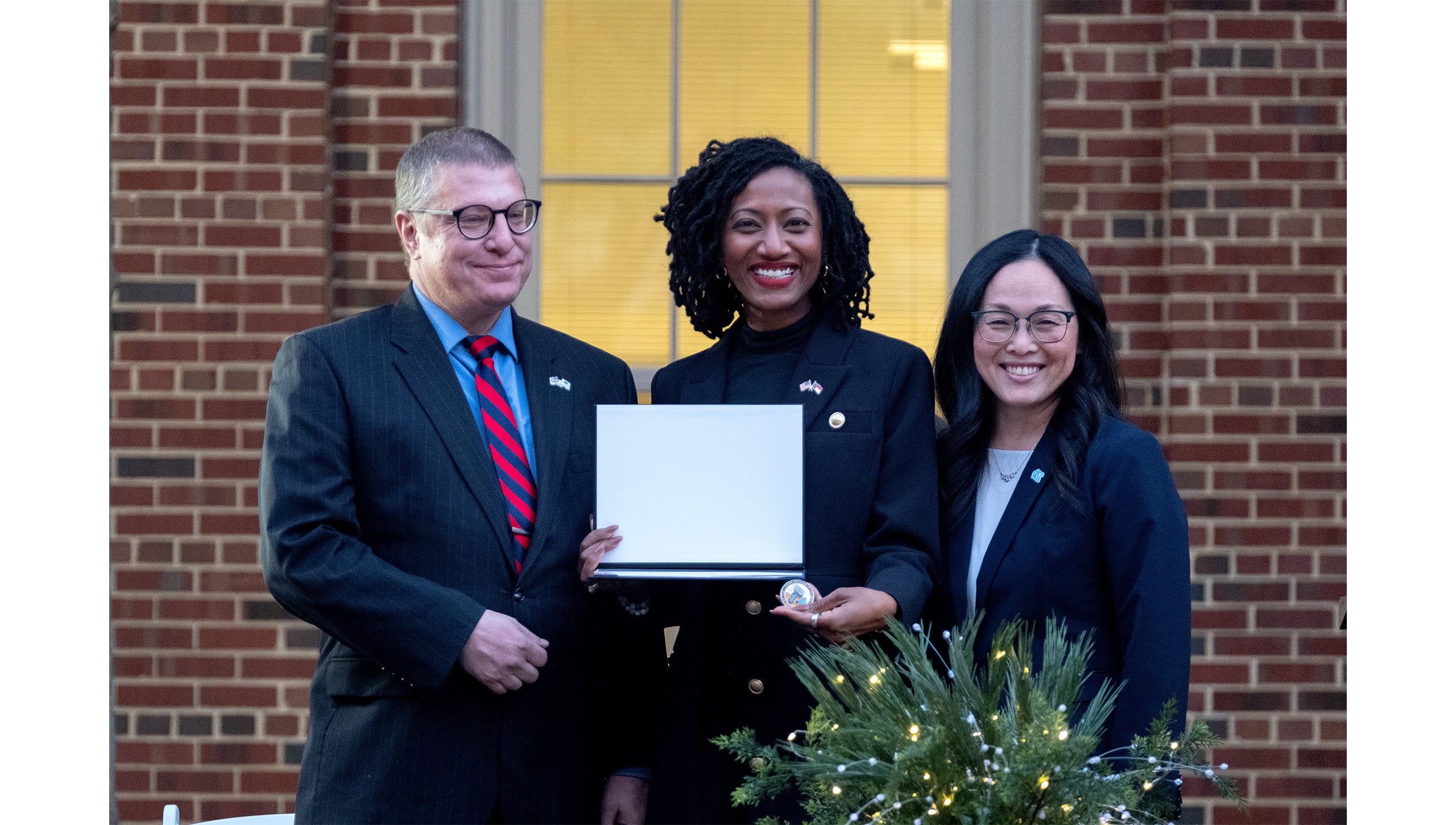 Rob Palermo and Desirée Rieckenberg posing with Jocelyn Mitnaul Mallette while presenting her with a challenge coin from the UNC-Chapel Hill Military and Veteran Student Success Center at its grand opening.