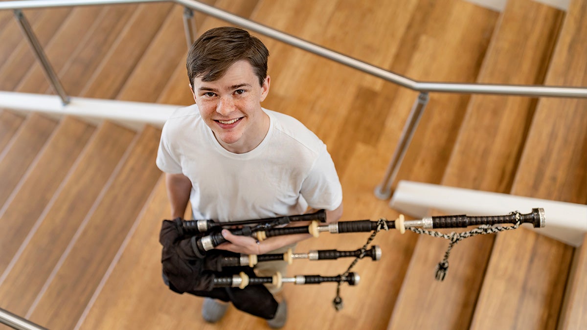 Daniel Caudill standing on stairs and looking upward for a portrait while holding a bagpipe.