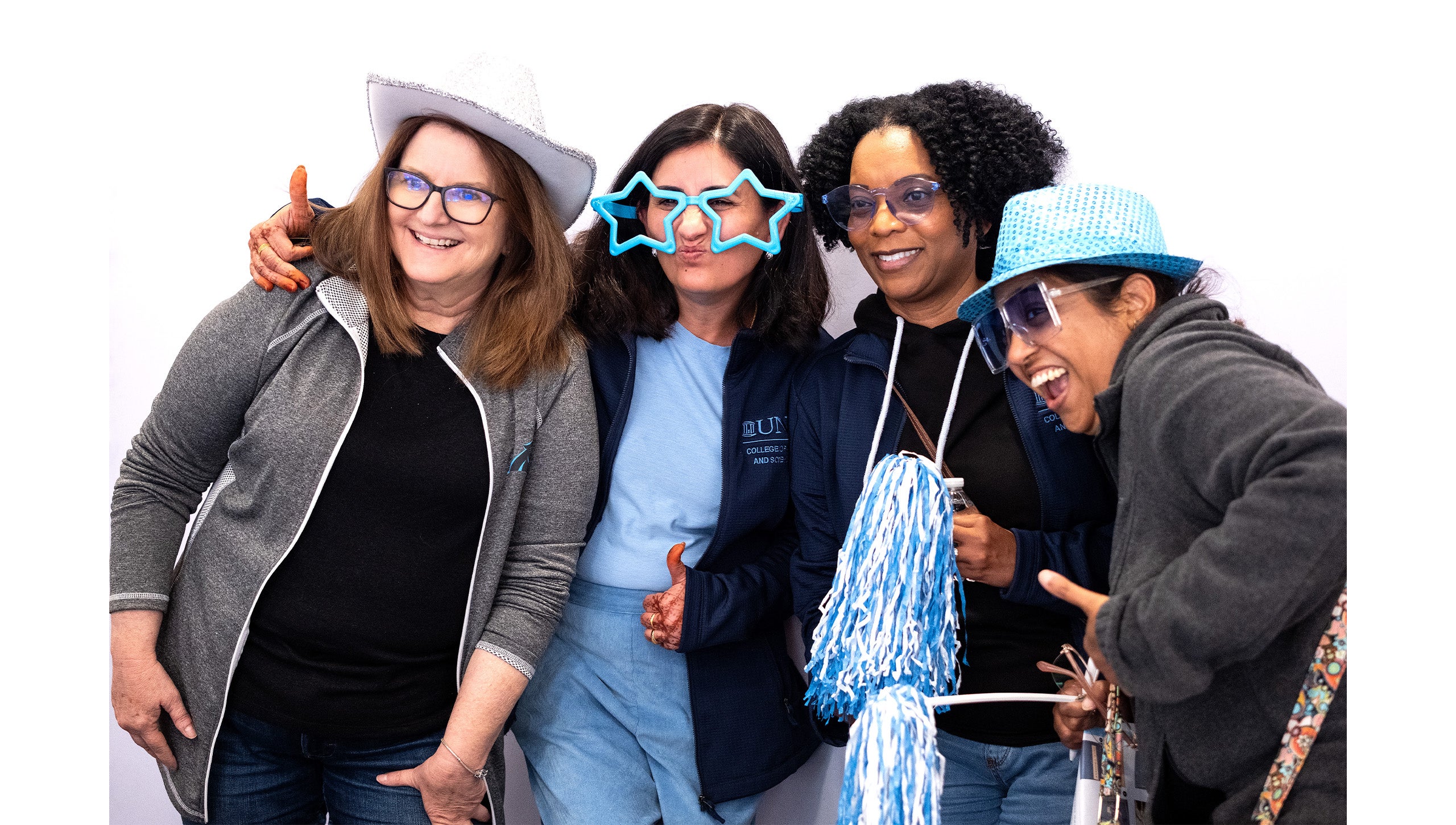 Four UNC-Chapel Hill employees posing for a group photo with various Carolina Blue props.