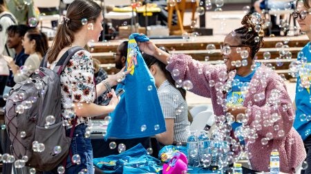 Bubbles floating in the air as a student is handed an Arts Everywhere T-shirt.