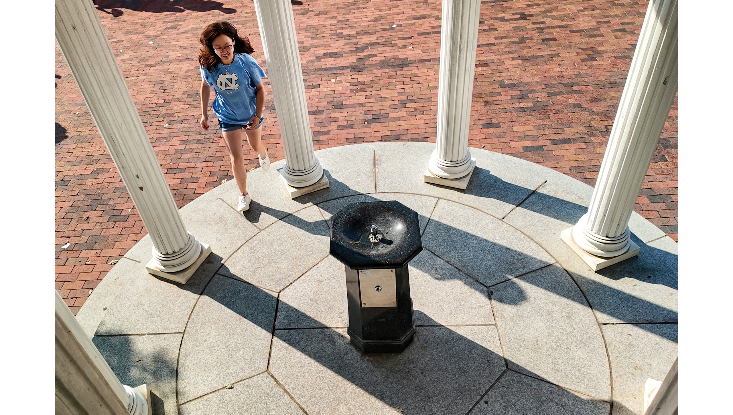 Aerial image of a UNC-Chapel Hill student smiling as she approaches the Old Well for her first sip.