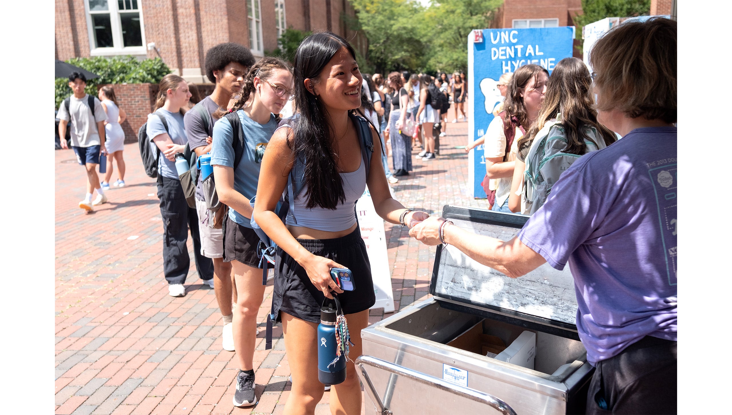UNC-Chapel Hill student smiling as she is handed a LocoPop by an employee in front of a long line of students near the Pit.