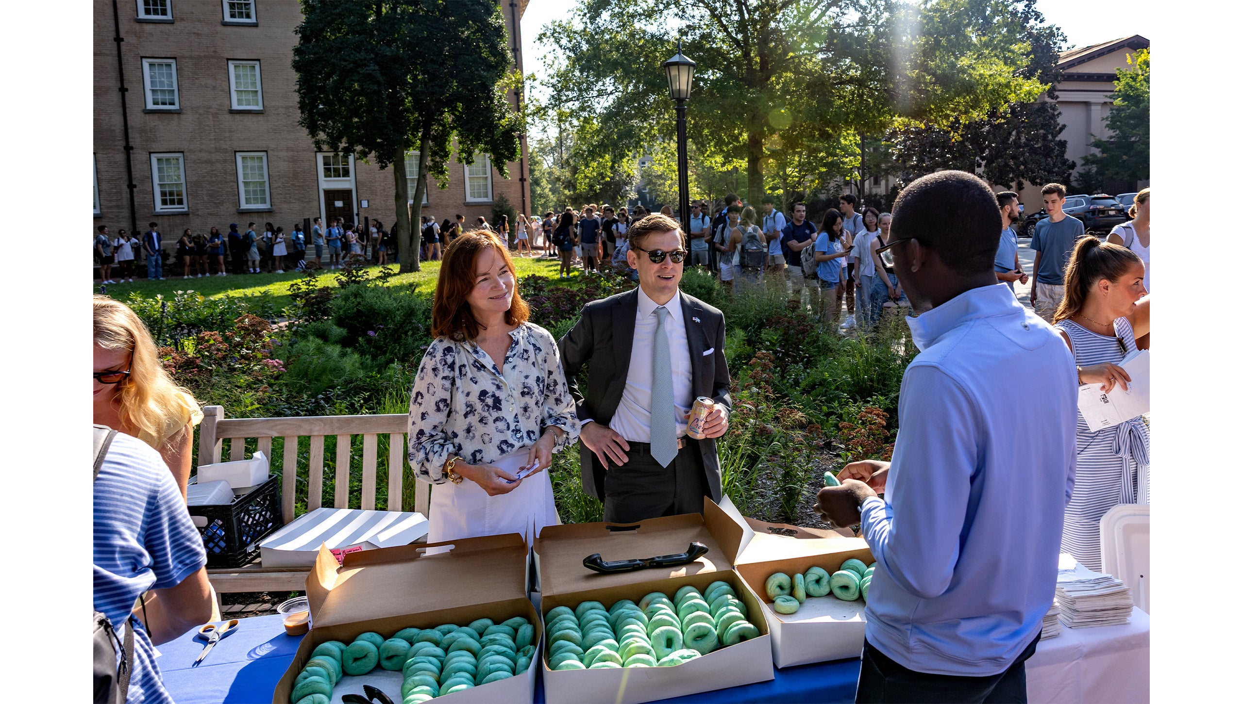 Chancellor Lee H. Roberts and his wife, Liza, speaking with a student as they hand out bagels near the Old Well. A long line of students waiting for their first sip is seen in the background.