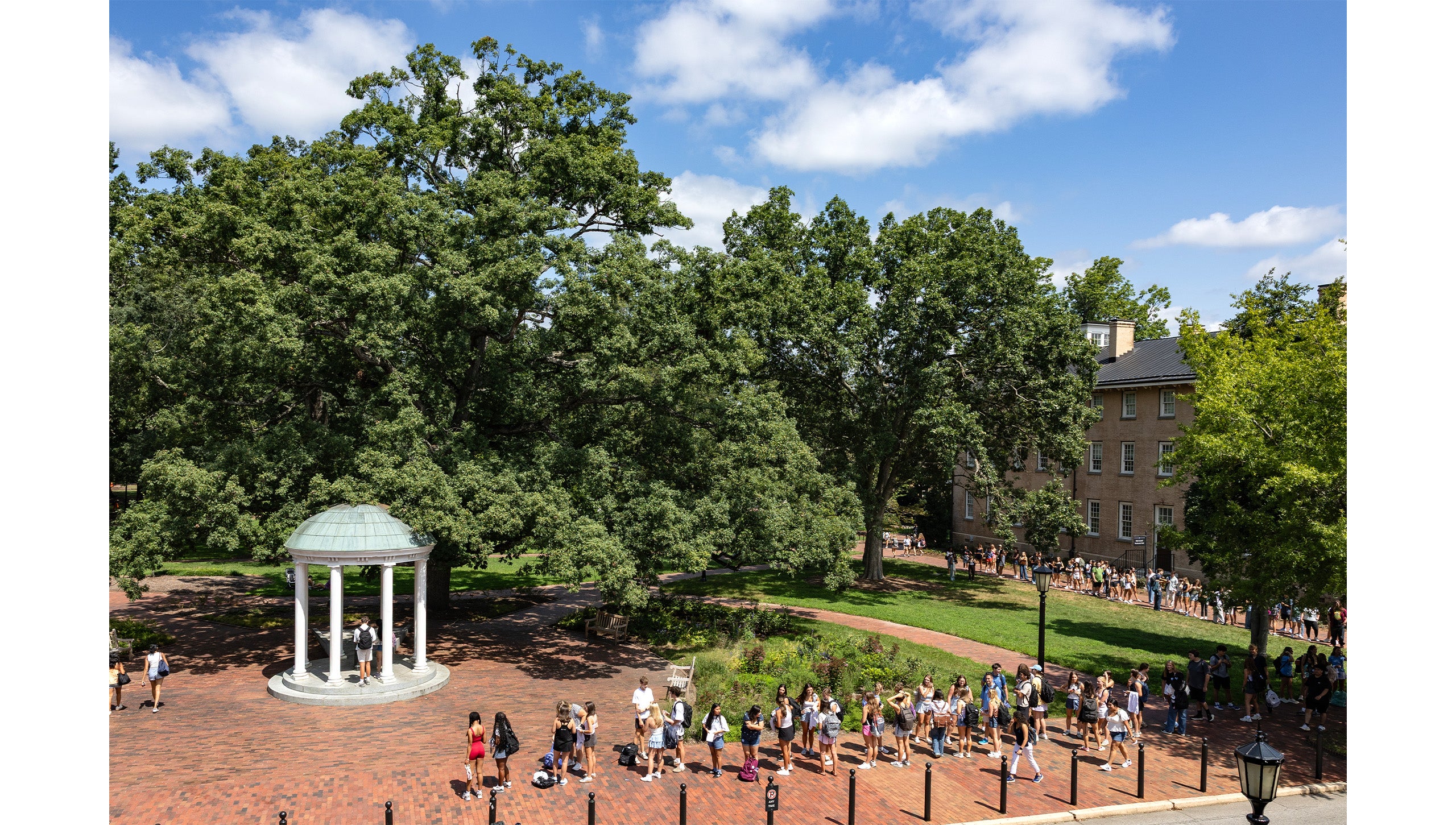 Aerial image from across Cameron Avenue of students waiting in line near the Old Well to take their first sip.