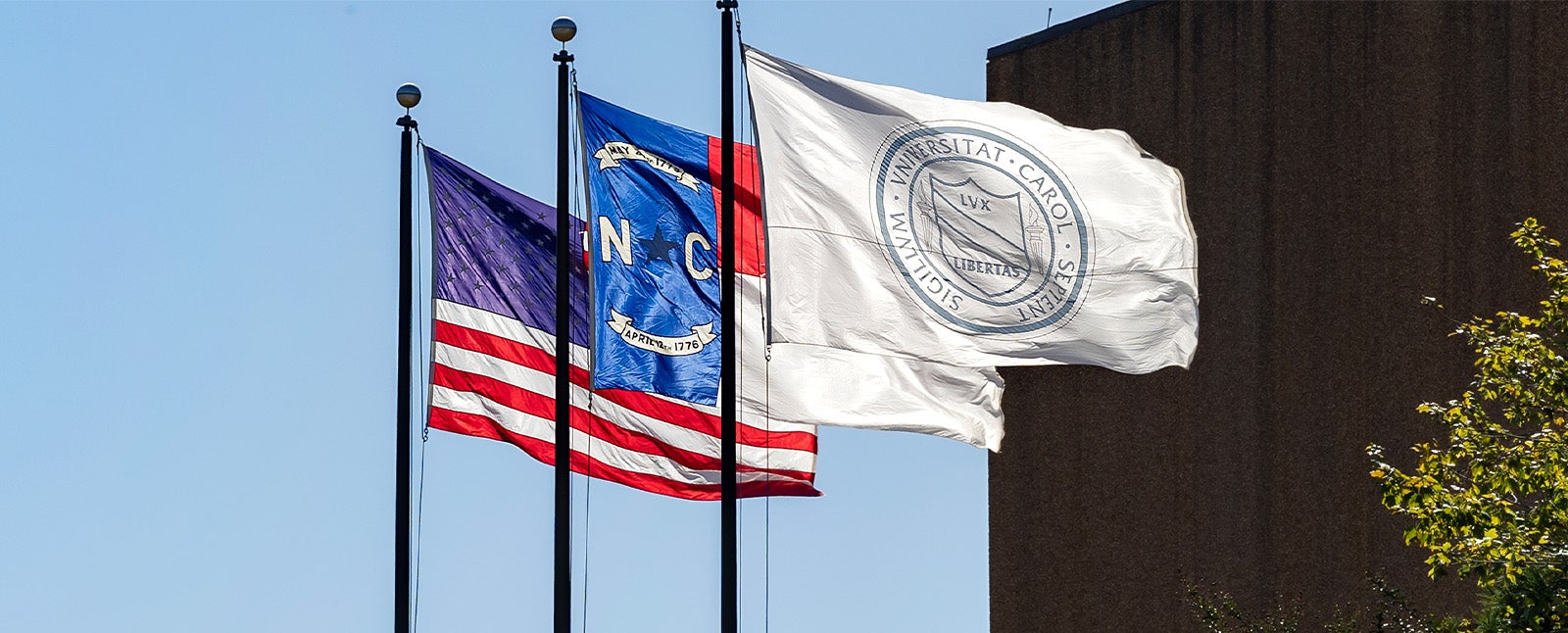 The American flag, the state of North Carolina flag and a UNC-Chapel Hill flag with the University seal flying on a sunny day outside the Dean E. Smith Center.