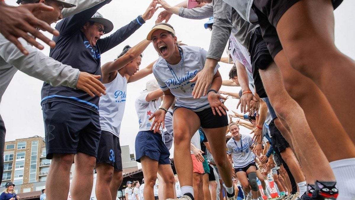Frisbee player runs through tunnel of supporters holding hands above after victory.