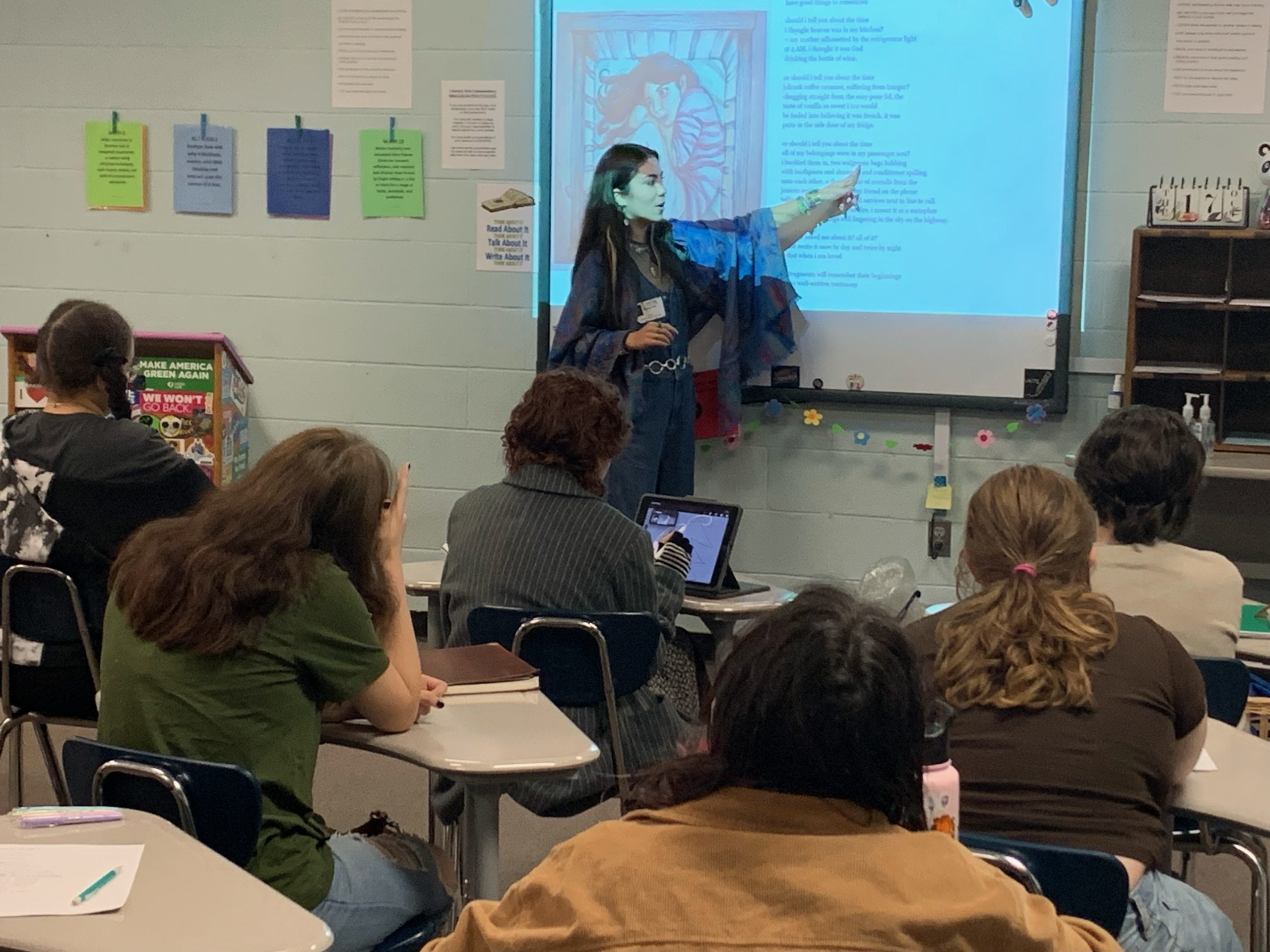 Mel Dalili in front of a high school class room teaching poetry to students.