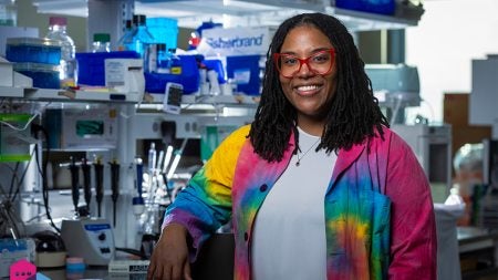 Jasmine King wearing a white shirt and rainbow-colored blazer in front of research equipment.