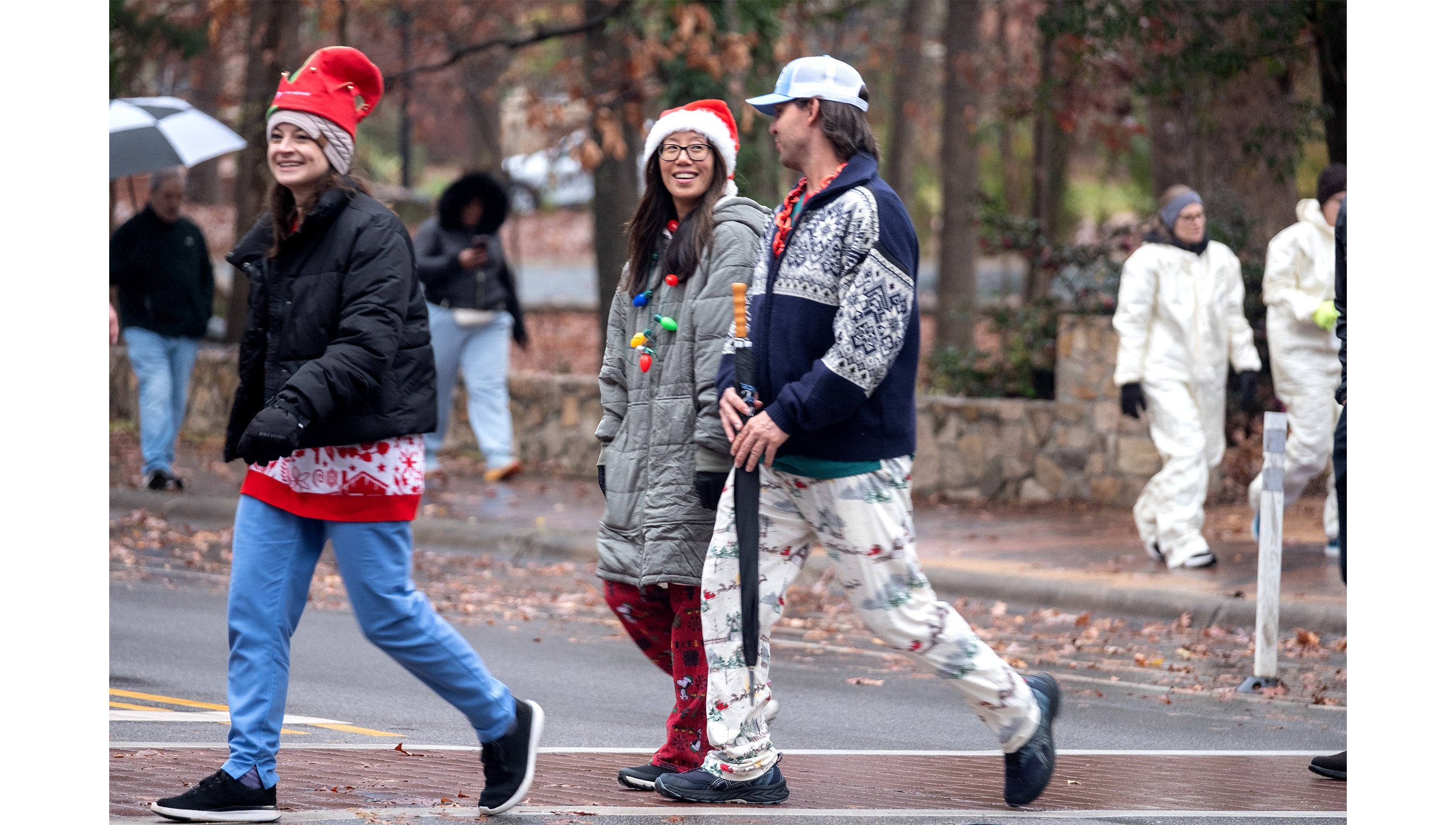 Three UNC-Chapel Hill employees in festive holiday costumes and gear crossing South Road at a crosswalk during the Jingle Bell Jog.