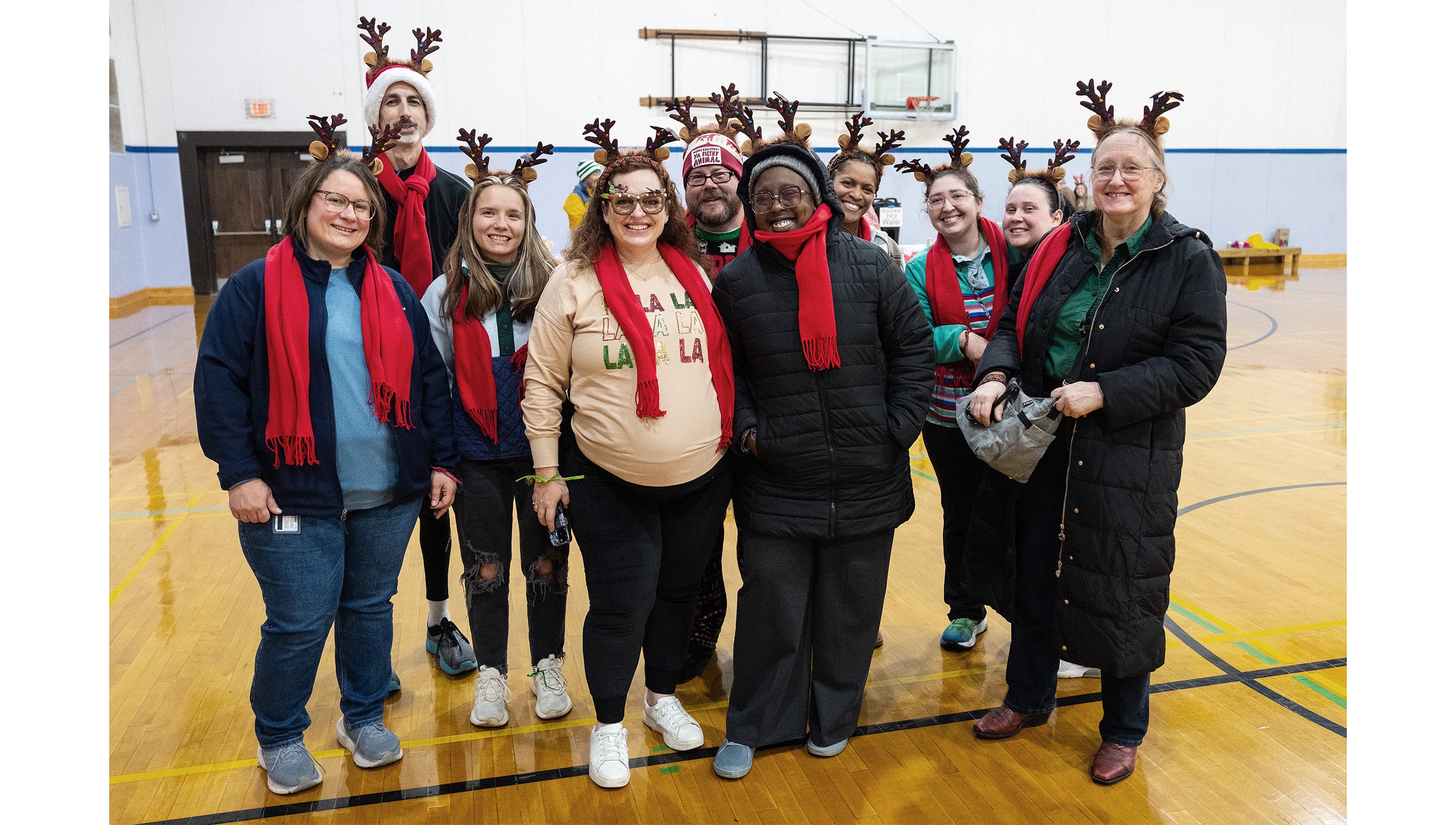 Ten UNC-Chapel Hill employees in festive reindeer costumes posing for a group photo inside a gym at Fetzer Hall during the Jingle Bell Jog.