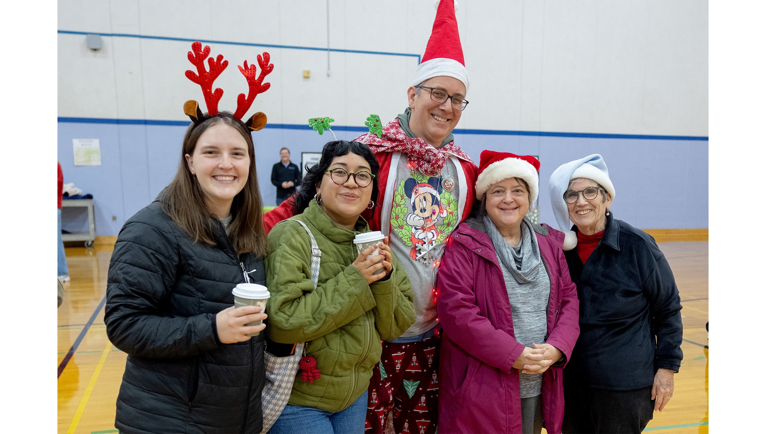 Five UNC-Chapel Hill employees in festive costumes posing for a group photo inside a gym at Fetzer Hall during the Jingle Bell Jog.