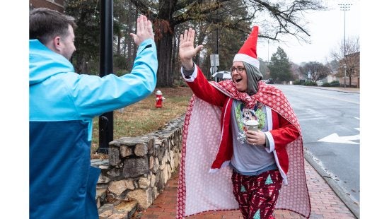 A man wearing a Mickey Mouse Christmas shirt, an elf hat, Christmas tree pajama pants and a Christmas cape high-fiving a man during the UNC-Chapel Hill Jingle Bell Jog.