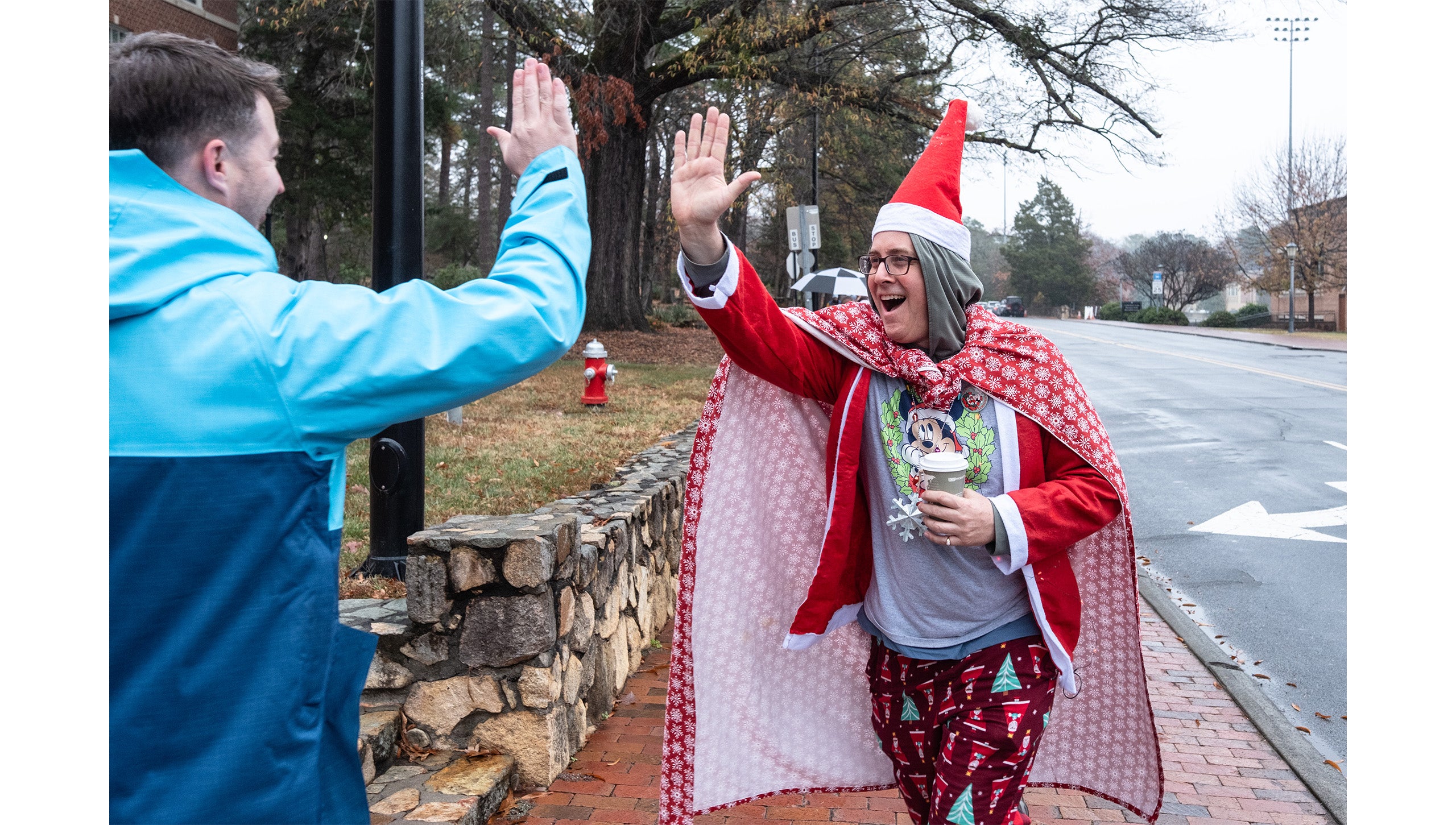 A man wearing a Mickey Mouse Christmas shirt, an elf hat, Christmas tree pajama pants and a Christmas cape high-fiving a man during the UNC-Chapel Hill Jingle Bell Jog.