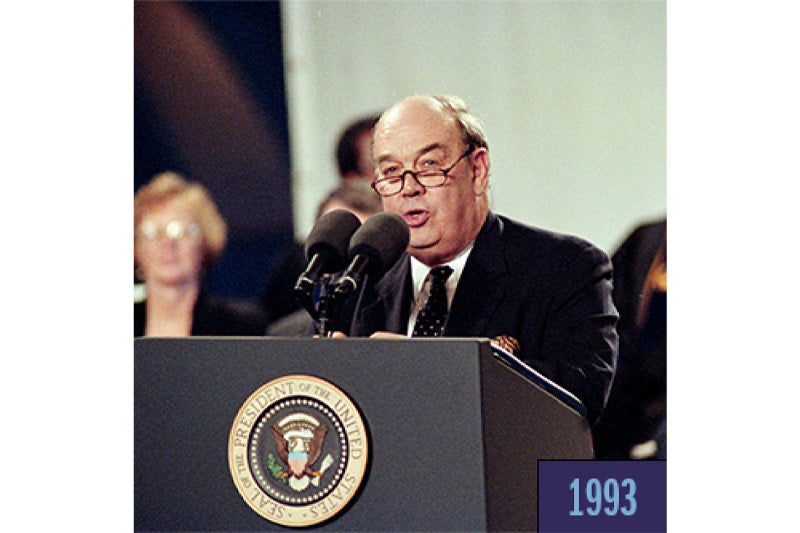 A man, Charles Kuralt, giving a speech and speaking into microphones at a podium.
