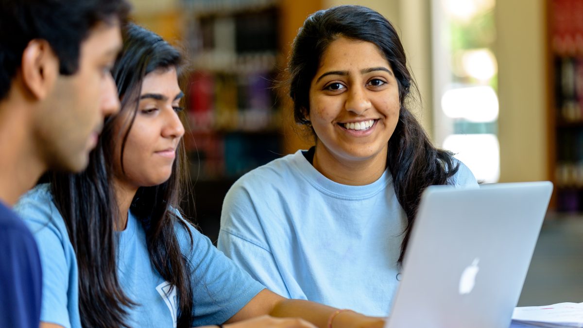 A male student and two female students work on a computer in a U.N.C. library.