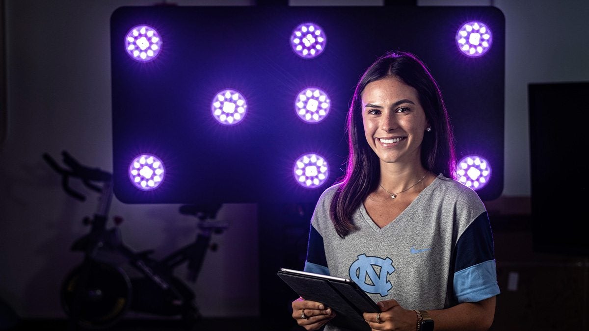UNC-Chapel Hill student researcher Mia Laws posing for a portrait, seen with a digital tool she uses in a research study measuring response times.