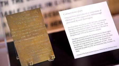 Close-up image of the bronze commemorative plaque created for the Old East cornerstone at UNC-CHapel Hill next to a description of the plaque headlined 