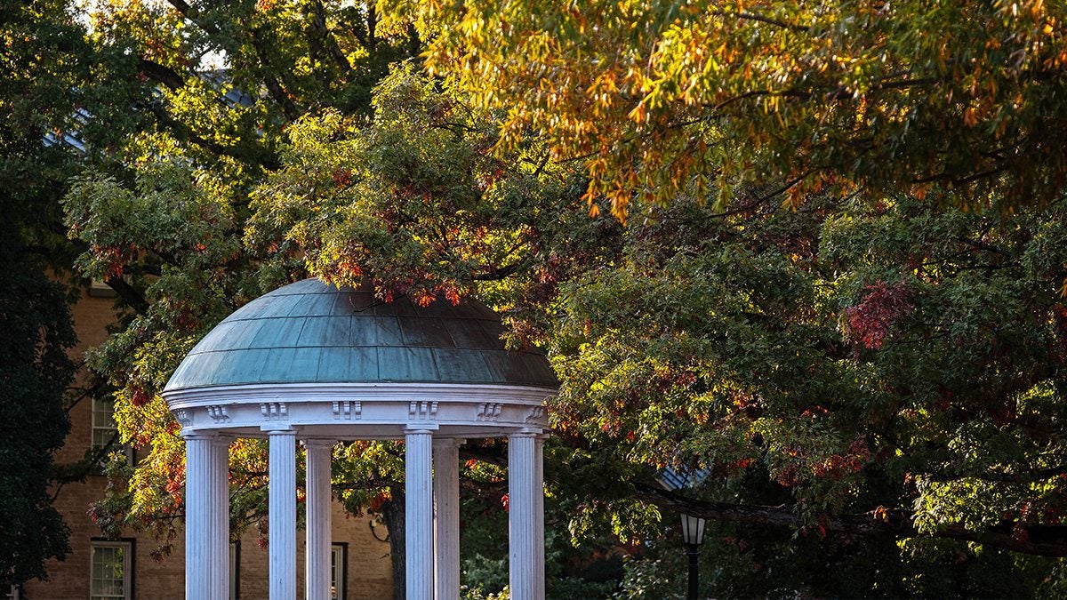 The Old Well, surrounded by trees with fall-colored leaves on them, on a sunny day.