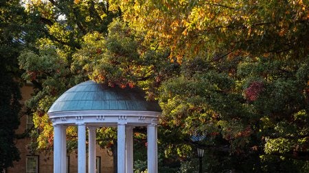 The Old Well, surrounded by trees with fall-colored leaves on them, on a sunny day.