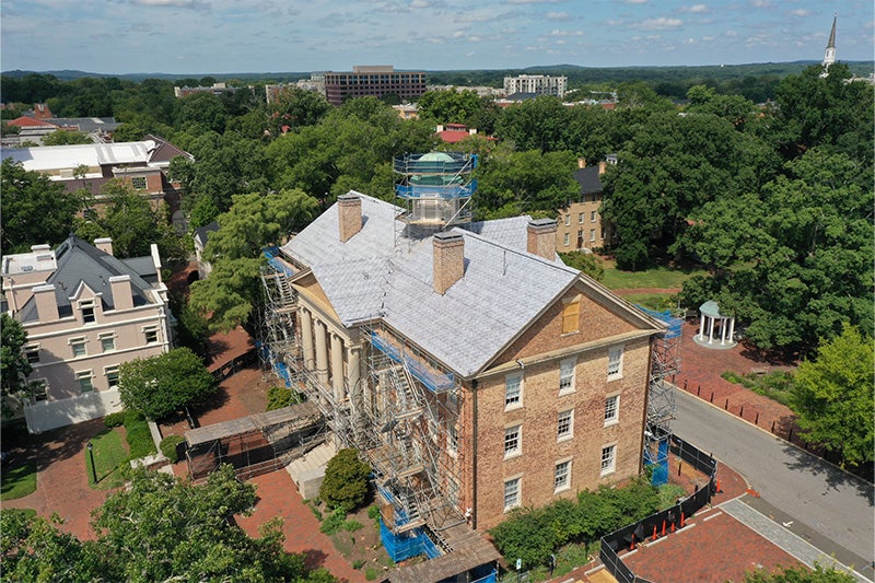 Sky view of South Building from a diagonal angle on a sunny day on the campus of UNC-Chapel Hill. Scaffolding is seen around the building and on its roof, and the Old Well is seen behind the building.