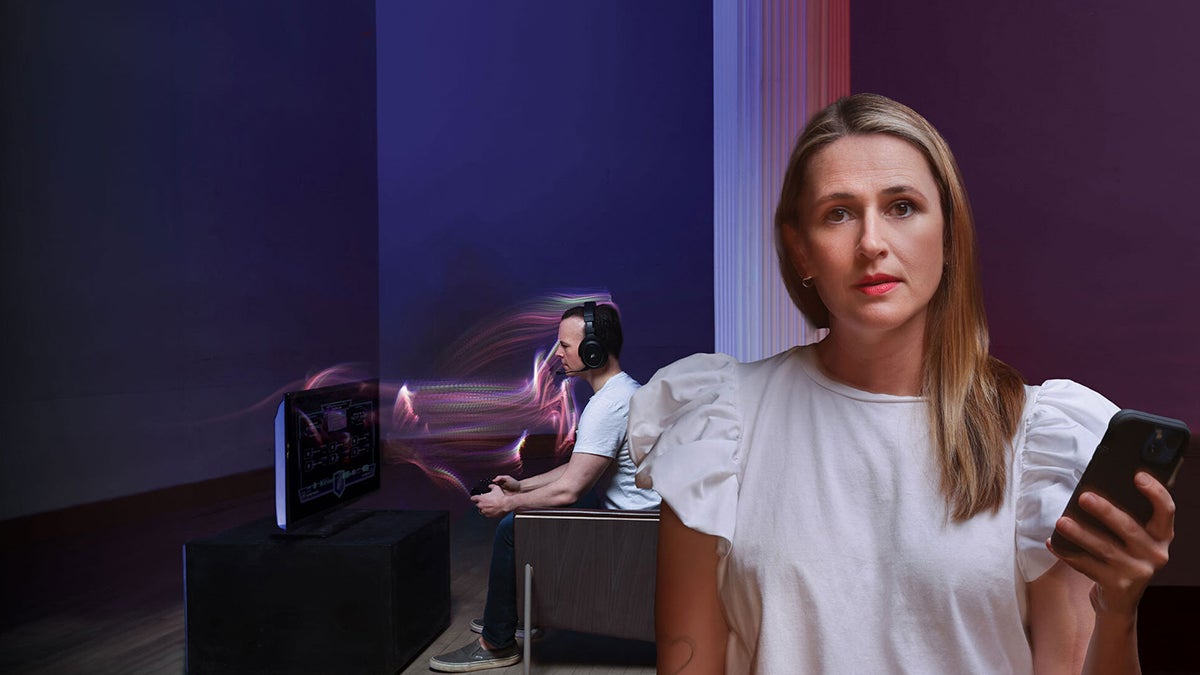 Woman in foreground looking into camera with a look of concern, while man behind her plays a video game.