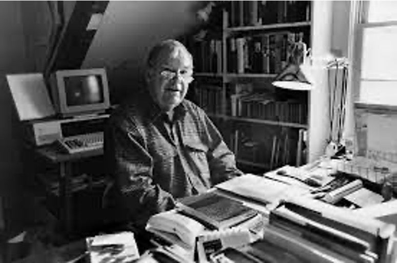 Tom Wicker sits at his desk, with papers in front of him and a computer behind him.