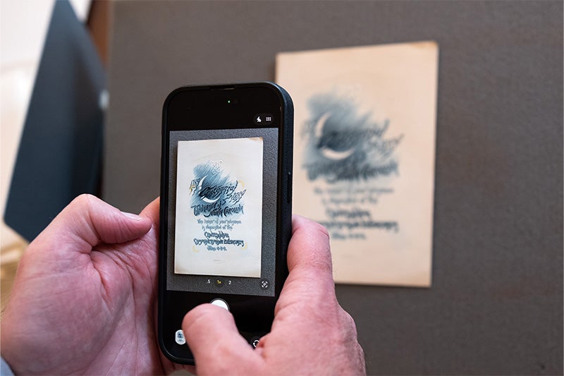 Hand of Nick Graham using an iPhone camera to take a picture of an invitation to UNC-Chapel Hill’s centennial commencement in 1889.