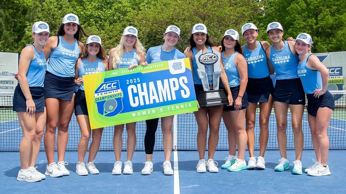 Carolina women's tennis players pose with the ACC championship trophy and a banner that says 