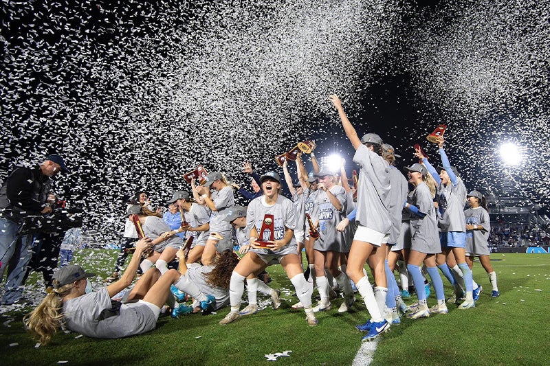 UNC women's soccer team celebrating with trophy as confetti fills the air following their national championship victory.