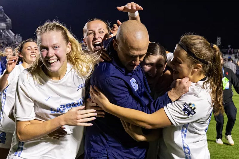 UNC women's soccer players crowding coach Damon Nahas in celebration following their national championship victory.