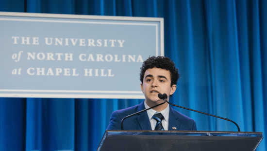 Student body president Adolfo stands at a podium talking to a group of people at U.N.C. campus.