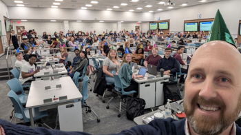 Kris Jordan wearing a green party hat, takes a group selfie with his class that surprised him with their party hats on his birtday.
