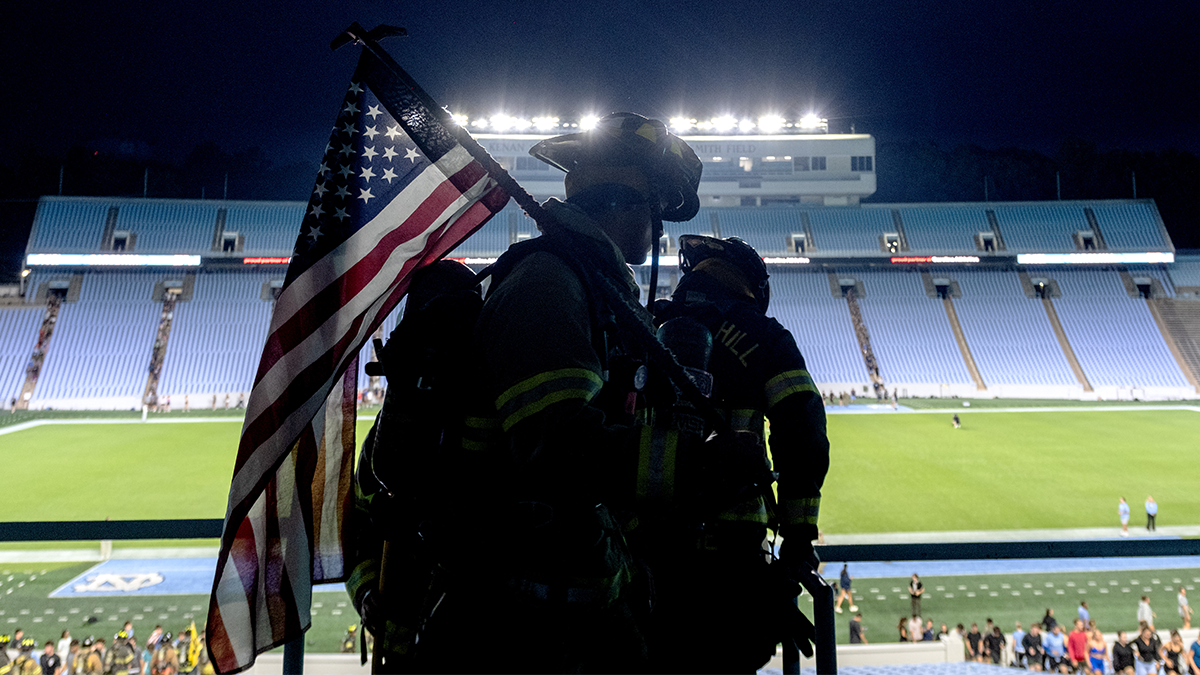 Firefighters silhouetted against Kenan stadium's field.