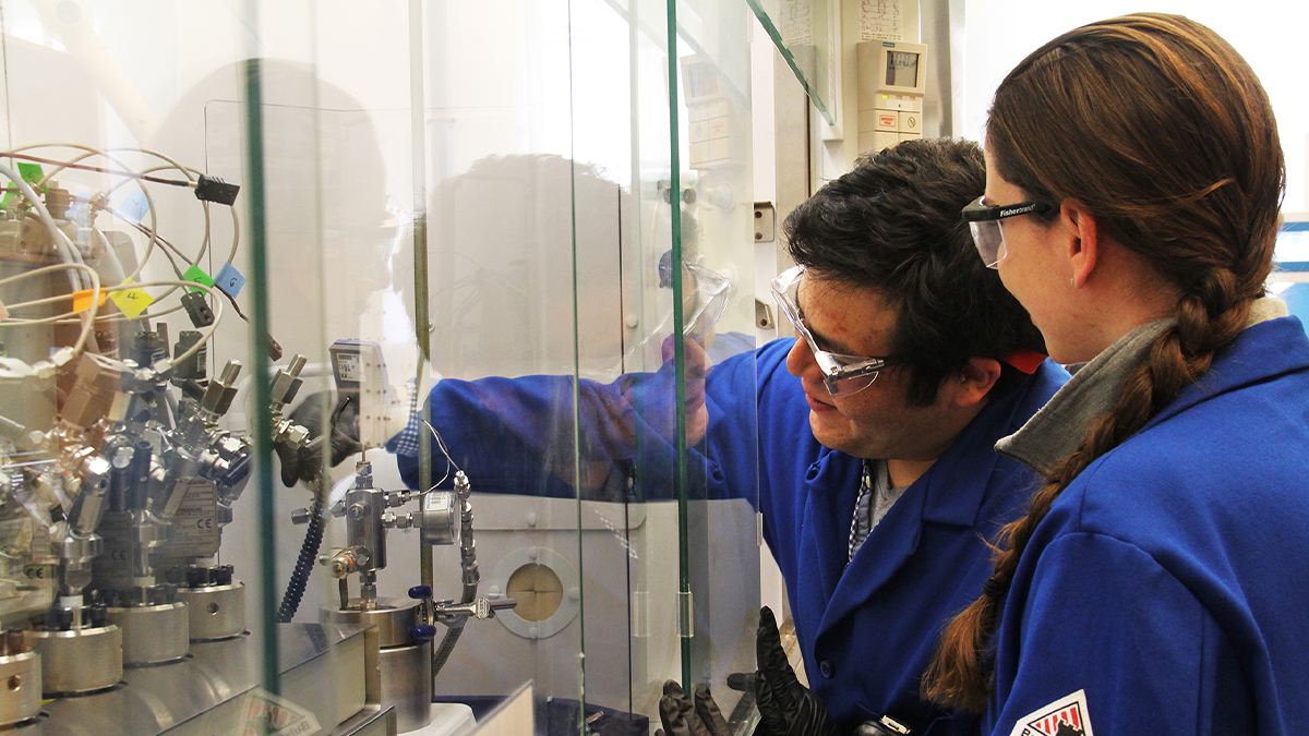 Researchers working in a lab wearing lab jackets and working on the other side of glass.