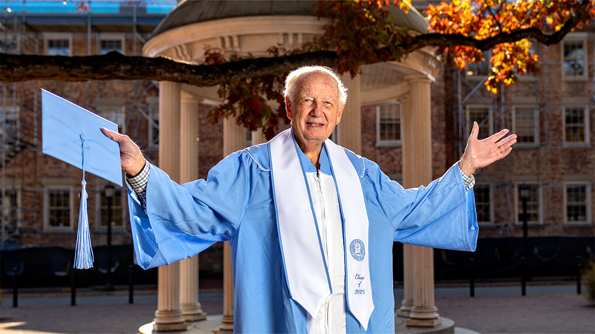Dr. David Kelly wearing commencement robes in front of the Old Well.