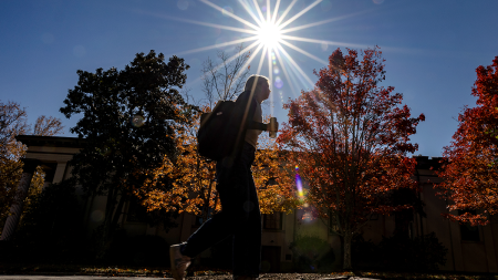 Student walking on campus holding coffee.