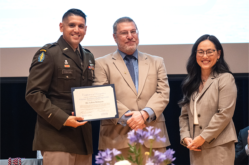 LeBon Hobayan on stage with two UNC-Chapel Hill administrators and receiving a diploma at the Red, White and Carolina Blue ceremony.