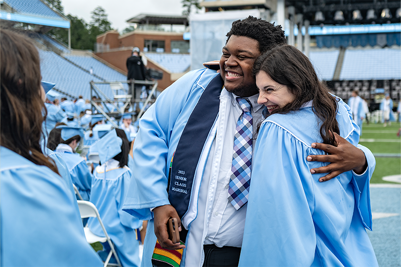 A student marshal from the class of 2025 embraces a fellow student at the summer graduation as they pose for a photo.