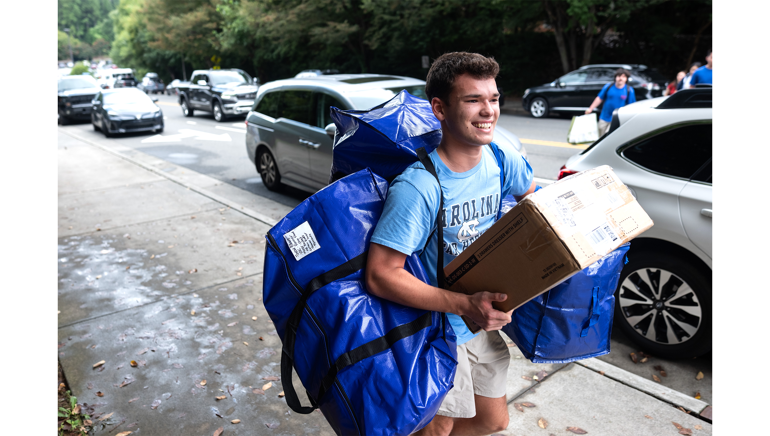 Student with big bags slung over shoulder and holding packing box.