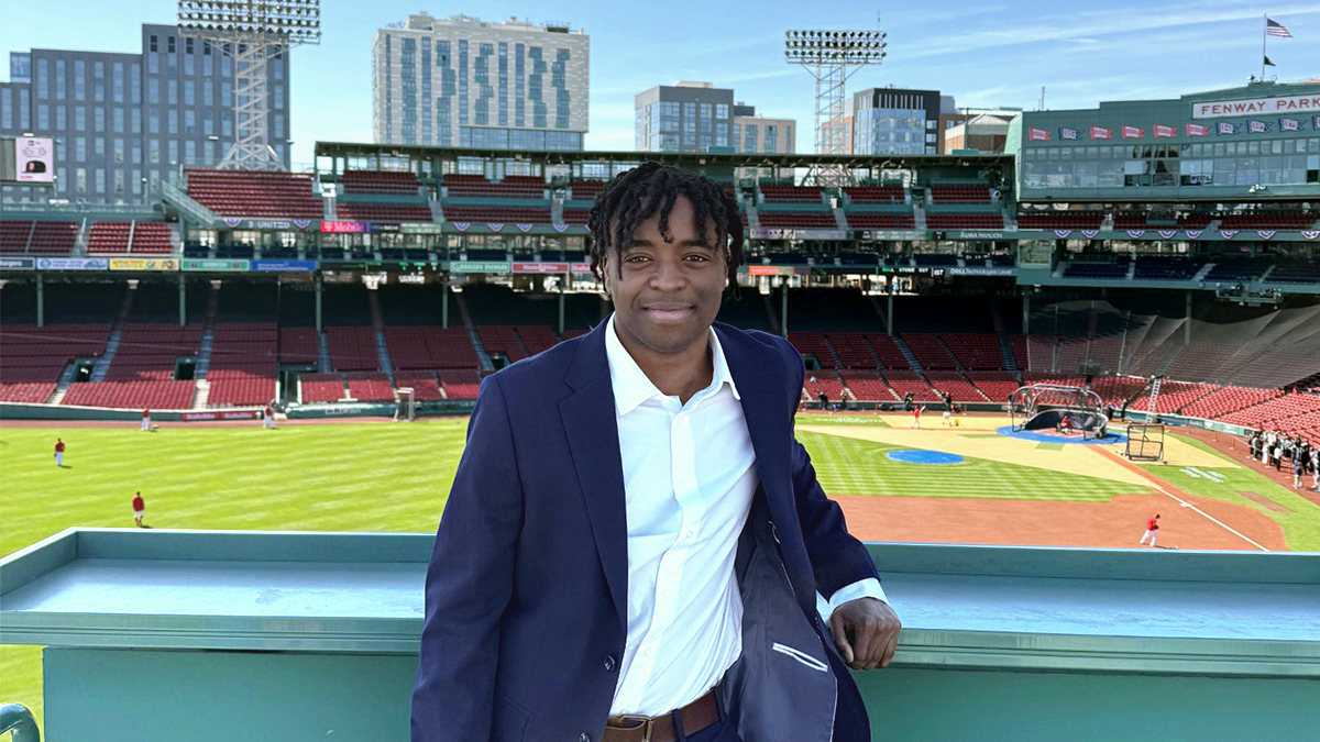 Neil-Pierre Louis leaning against green railing in left field of Fenway Park in Boston.