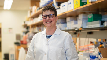 Samantha Pattenden in a lab coat smiles for a photo while she stands in her lab on U.N.C. campus.
